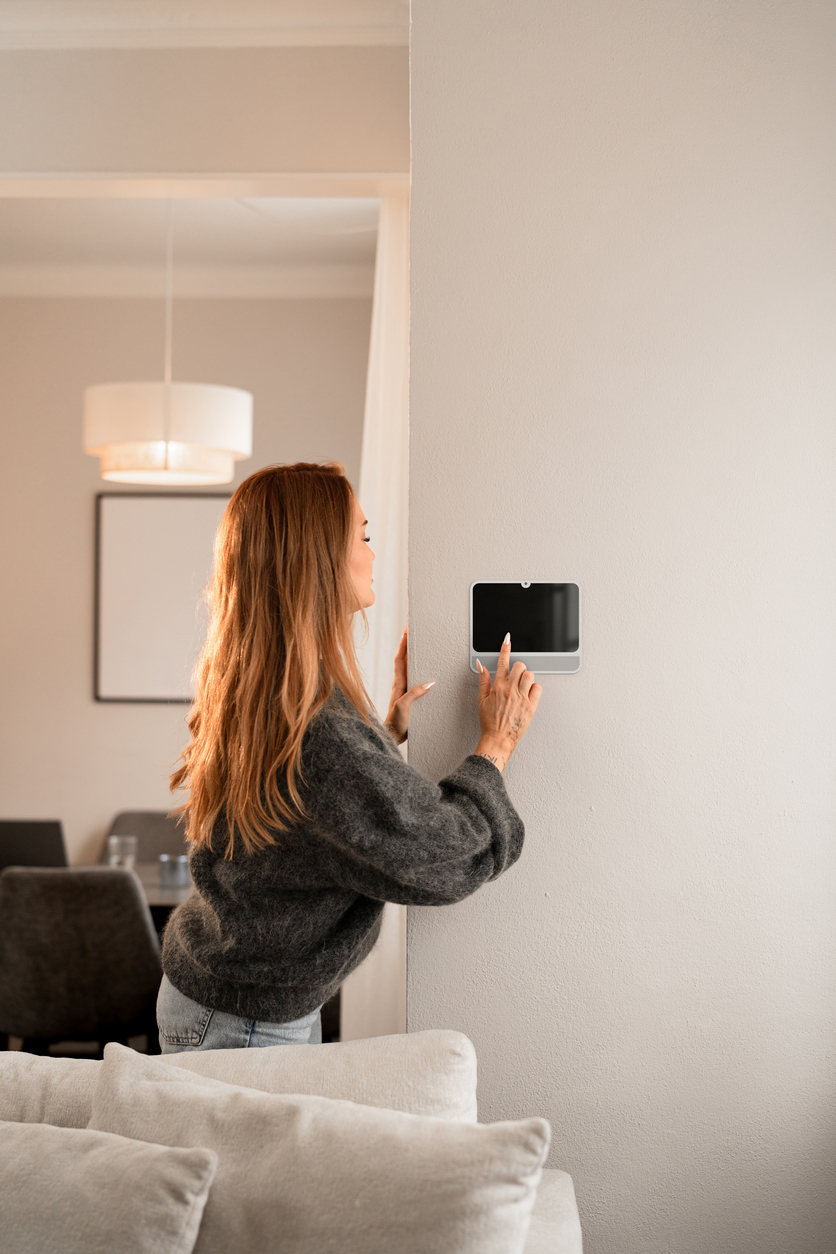 Woman adjusts a wall mounted smart home control panel in a modern living room setting